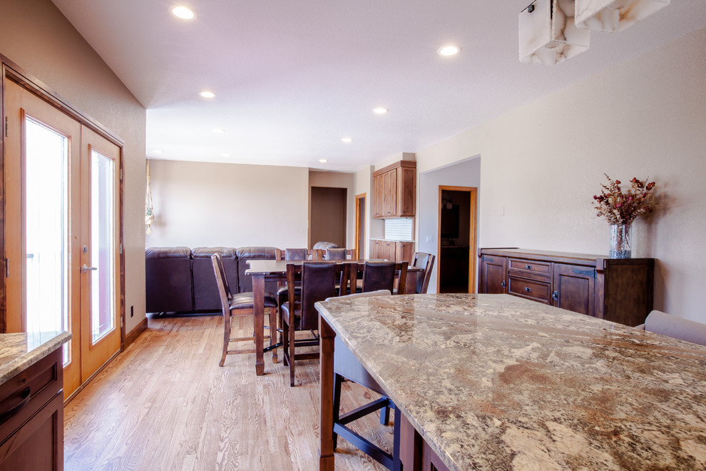 Example of a mid-sized mountain style u-shaped medium tone wood floor and brown floor enclosed kitchen design in Omaha with an undermount sink, shaker cabinets, dark wood cabinets, granite countertops, beige backsplash, travertine backsplash, stainless steel appliances, an island and multicolored countertops