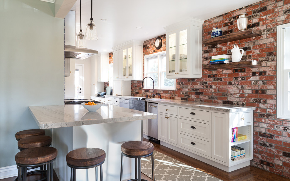 Photo of a mid-sized country galley eat-in kitchen in Sacramento with a farmhouse sink, recessed-panel cabinets, white cabinets, quartzite benchtops, red splashback, stone tile splashback, stainless steel appliances, medium hardwood floors, with island and brown floor.