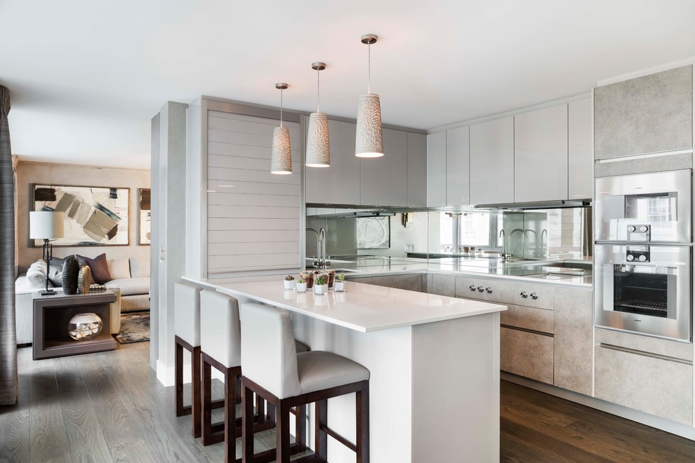 Mid-sized contemporary l-shaped eat-in kitchen in London with flat-panel cabinets, grey cabinets, mirror splashback, dark hardwood floors, a peninsula, brown floor, an undermount sink, laminate benchtops and stainless steel appliances.