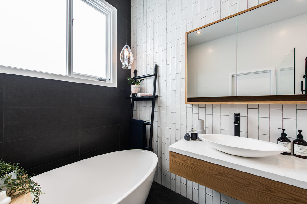 Photo of a contemporary kids bathroom in Melbourne with furniture-like cabinets, medium wood cabinets, a freestanding tub, an open shower, a one-piece toilet, black and white tile, porcelain tile, porcelain floors, a vessel sink, engineered quartz benchtops and black floor.