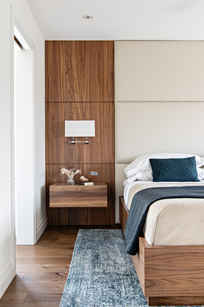 Cette image montre une grande chambre parentale design en bois avec un mur blanc et un sol en bois brun.