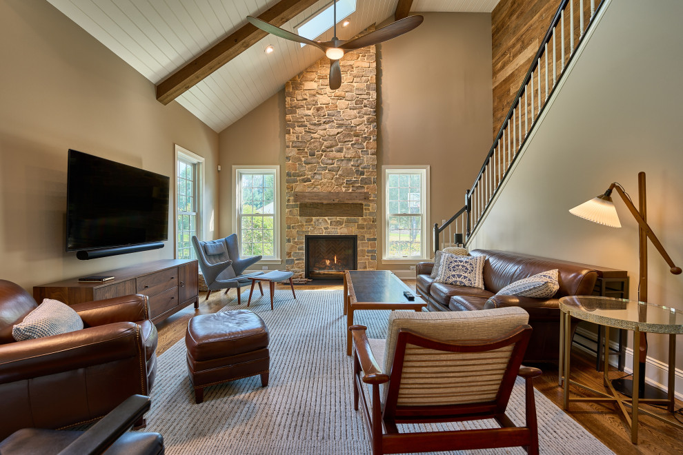 This is an example of a large traditional open plan living room in Philadelphia with beige walls, medium hardwood flooring, a standard fireplace, a stone fireplace surround, a wall mounted tv, brown floors, exposed beams and tongue and groove walls.