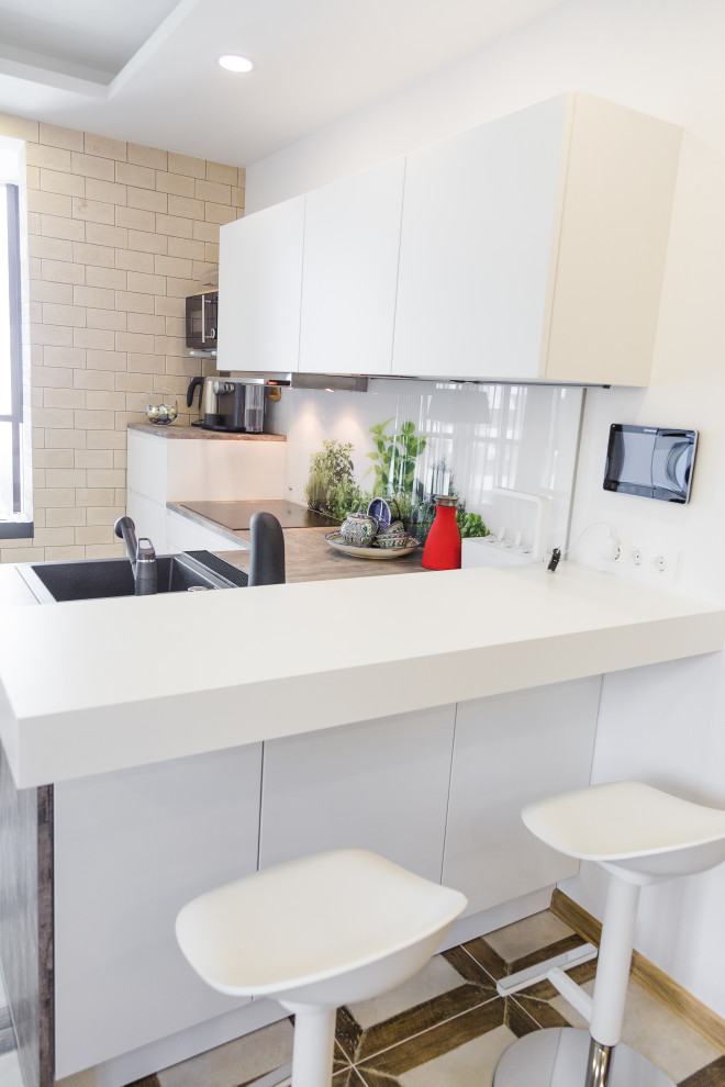 Photo of a small contemporary l-shaped kitchen in Other with a submerged sink, white cabinets, laminate countertops, white splashback, glass sheet splashback, black appliances and grey worktops.