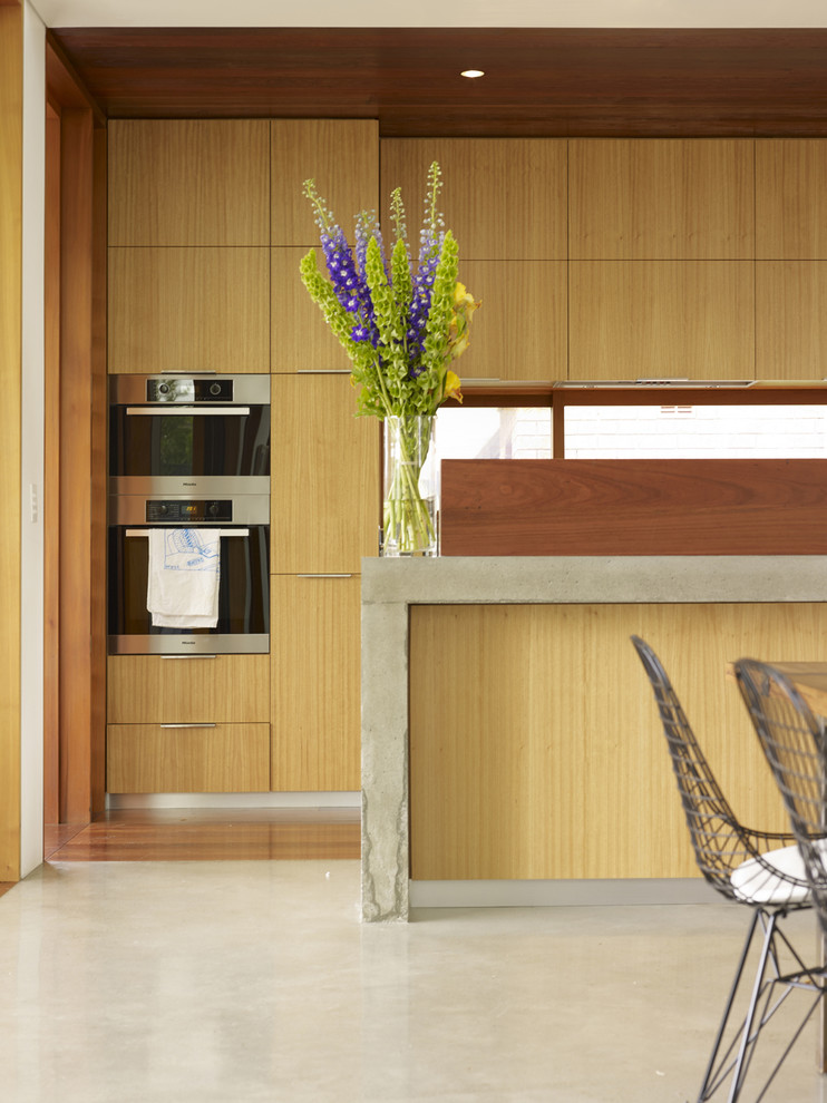 This is an example of a contemporary galley eat-in kitchen in Sydney with medium wood cabinets, concrete benchtops and with island.