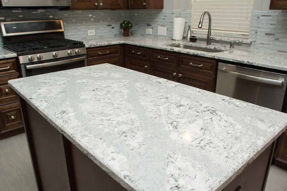 Mid-sized transitional l-shaped porcelain tile and gray floor open concept kitchen photo in Houston with a single-bowl sink, raised-panel cabinets, medium tone wood cabinets, quartz countertops, mosaic tile backsplash, stainless steel appliances, two islands and white backsplash