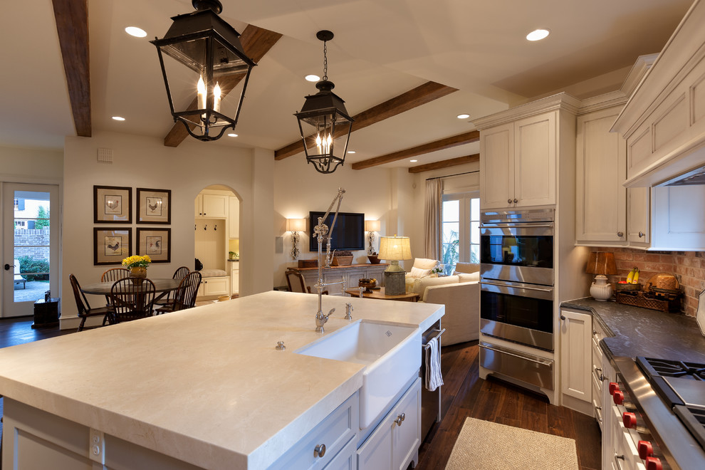 Design ideas for an expansive traditional u-shaped open plan kitchen in Houston with a farmhouse sink, recessed-panel cabinets, distressed cabinets, brick splashback, stainless steel appliances, dark hardwood floors, with island and brown floor.