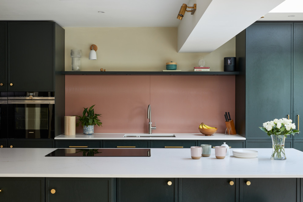 Inspiration for a large contemporary l-shaped kitchen/diner in Kent with recessed-panel cabinets, green cabinets, engineered stone countertops, pink splashback, glass sheet splashback, stainless steel appliances, an island and white worktops.