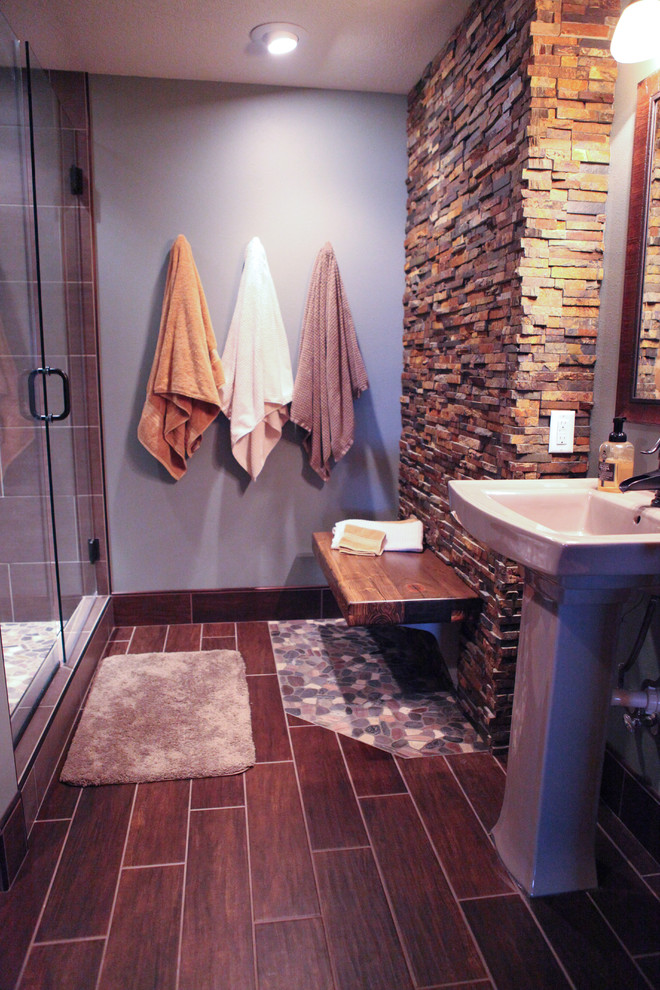 This is an example of a mid-sized country 3/4 bathroom in Other with open cabinets, dark wood cabinets, a corner shower, a two-piece toilet, multi-coloured tile, pebble tile, blue walls, porcelain floors and a pedestal sink.