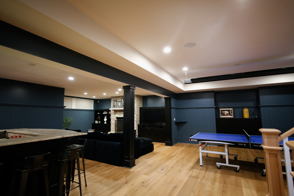 Inspiration pour un grand sous-sol traditionnel enterré avec un bar de salon, un mur bleu, parquet clair, une cheminée standard et un manteau de cheminée en pierre.