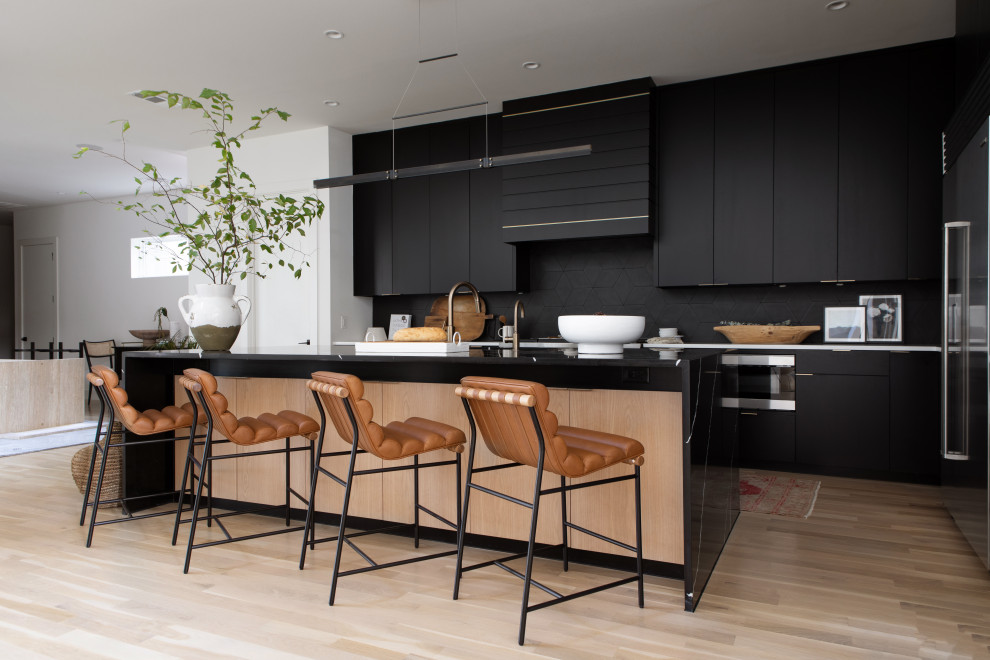 This is an example of a contemporary l-shaped open plan kitchen in Dallas with flat-panel cabinets, black cabinets, quartzite benchtops, black splashback, ceramic splashback, stainless steel appliances, light hardwood floors, with island and white benchtop.