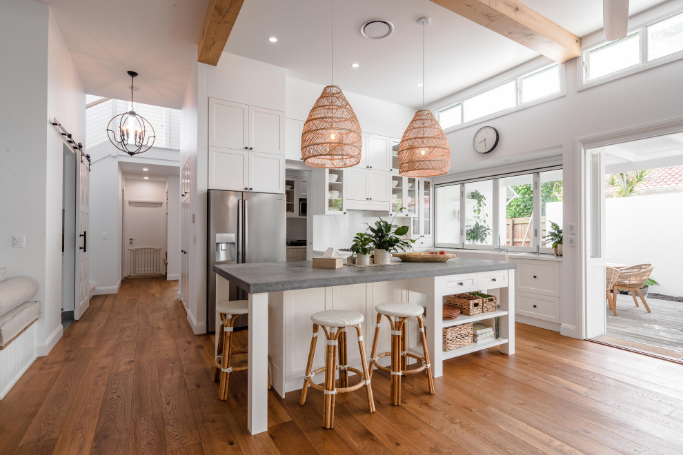 Design ideas for a large beach style l-shaped open plan kitchen in Sunshine Coast with a farmhouse sink, shaker cabinets, white cabinets, marble benchtops, grey splashback, with island, brown floor, grey benchtop, exposed beam and medium hardwood floors.