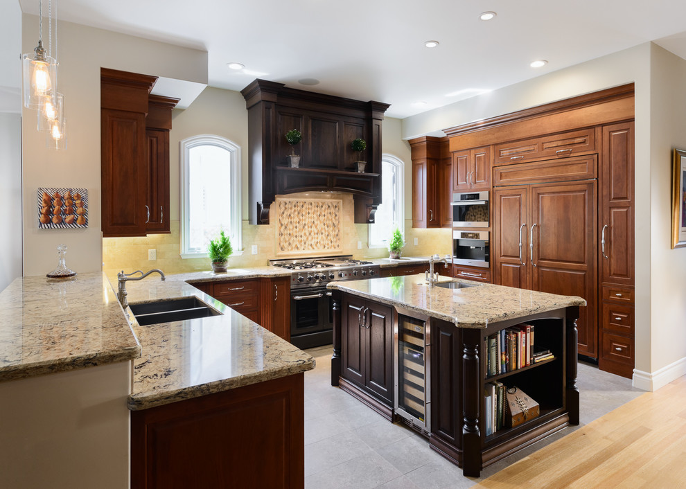 Photo of a large traditional u-shaped separate kitchen in Los Angeles with a double-bowl sink, raised-panel cabinets, dark wood cabinets, granite benchtops, beige splashback, ceramic splashback, panelled appliances, concrete floors, with island and grey floor.