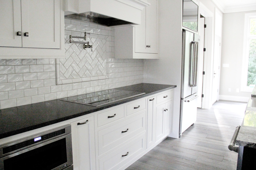 Example of a large single-wall light wood floor and brown floor eat-in kitchen design with recessed-panel cabinets, white cabinets, granite countertops, white backsplash, subway tile backsplash, stainless steel appliances and an island