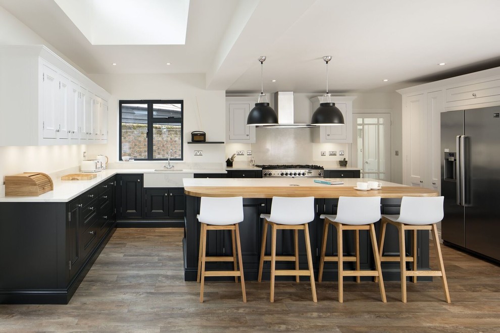 Photo of a transitional kitchen in Other with a farmhouse sink, recessed-panel cabinets, white splashback, stainless steel appliances, dark hardwood floors, with island, brown floor and white benchtop.