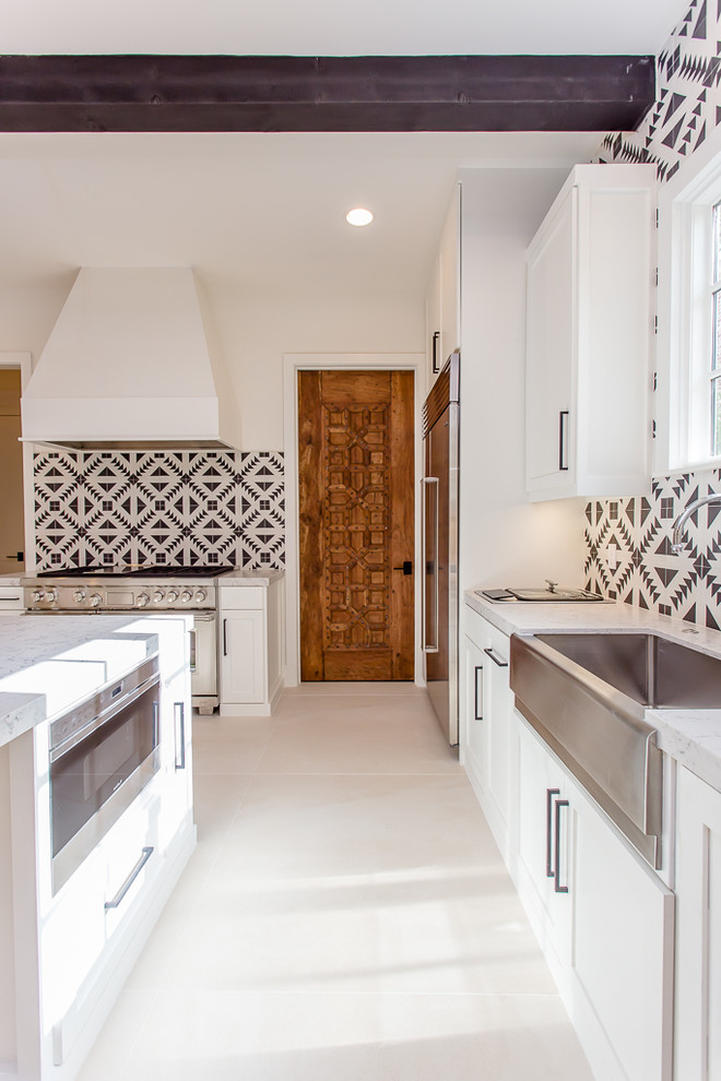 Photo of a large mediterranean l-shaped open plan kitchen in Houston with a farmhouse sink, shaker cabinets, white cabinets, solid surface benchtops, multi-coloured splashback, cement tile splashback, stainless steel appliances, ceramic floors and with island.