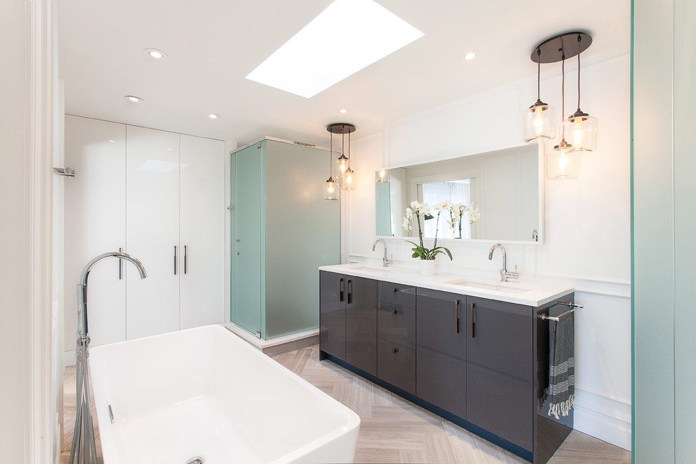 Large contemporary master bathroom in Ottawa with an undermount sink, flat-panel cabinets, grey cabinets, solid surface benchtops, a freestanding tub, white walls, a corner shower, light hardwood floors, brown floor and a hinged shower door.