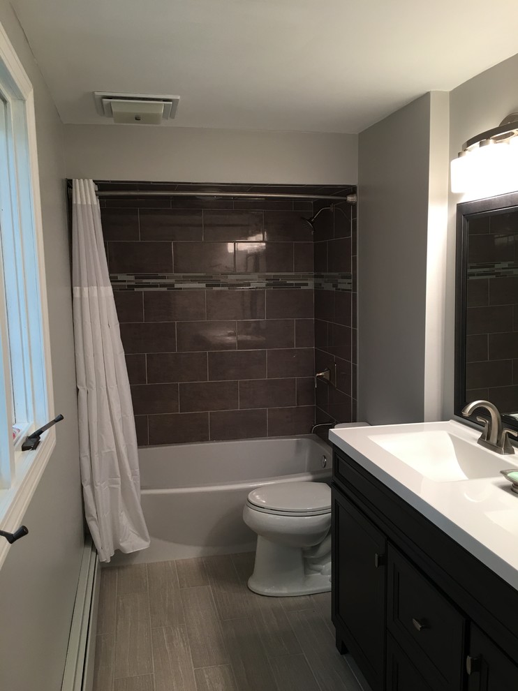 Design ideas for a small transitional master bathroom in Providence with recessed-panel cabinets, dark wood cabinets, an alcove tub, a shower/bathtub combo, a two-piece toilet, gray tile, porcelain tile, grey walls, porcelain floors, an integrated sink and solid surface benchtops.