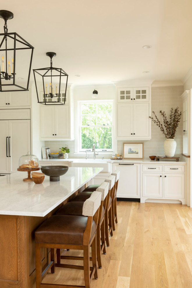 This is an example of a mid-sized beach style l-shaped eat-in kitchen in Minneapolis with a farmhouse sink, beaded inset cabinets, white cabinets, quartz benchtops, beige splashback, ceramic splashback, stainless steel appliances, light hardwood floors, with island, white benchtop and coffered.