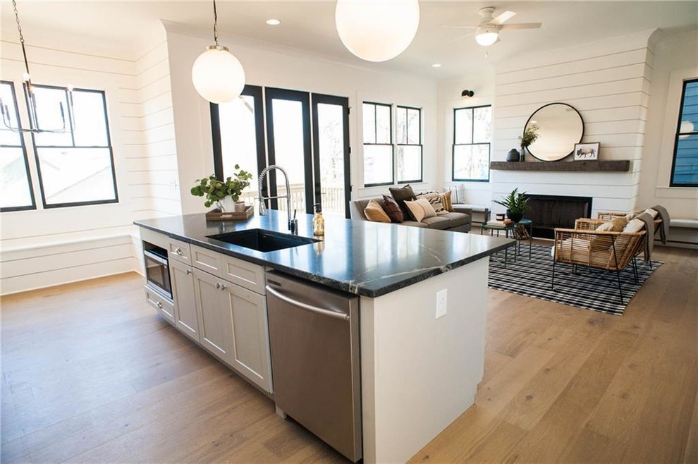 This is an example of a mid-sized transitional l-shaped open plan kitchen in Miami with an undermount sink, shaker cabinets, white cabinets, onyx benchtops, white splashback, timber splashback, stainless steel appliances, light hardwood floors, with island, beige floor and black benchtop.