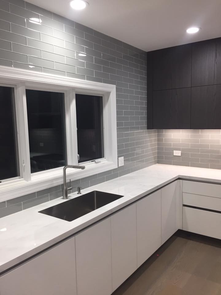 Example of a large transitional medium tone wood floor and brown floor kitchen design in Chicago with an undermount sink, flat-panel cabinets, black cabinets, quartzite countertops, gray backsplash, subway tile backsplash and stainless steel appliances