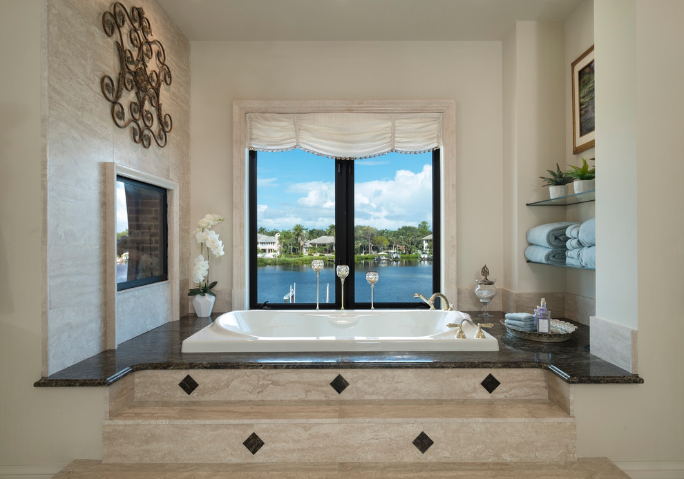 Photo of a large mediterranean master bathroom in Miami with furniture-like cabinets, a drop-in tub, beige tile, stone slab, beige walls, travertine floors, a drop-in sink, marble benchtops and beige floor.