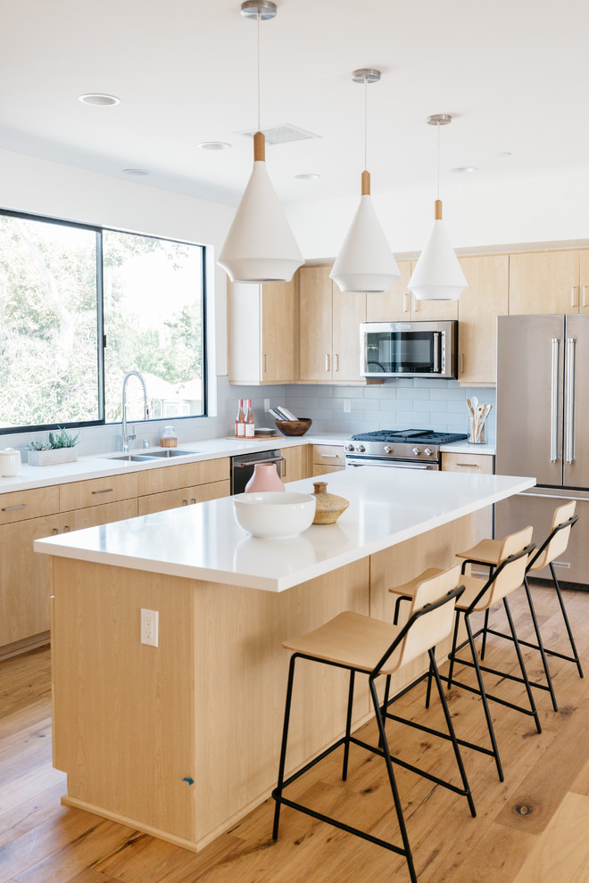 Inspiration for a contemporary l-shaped kitchen in Los Angeles with a double-bowl sink, flat-panel cabinets, light wood cabinets, stainless steel appliances, medium hardwood floors, with island, brown floor and white benchtop.