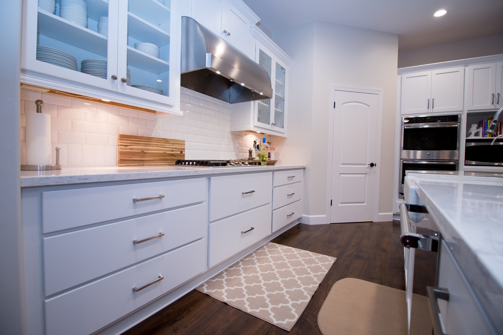 Open concept kitchen - large transitional l-shaped dark wood floor open concept kitchen idea with a farmhouse sink, shaker cabinets, white cabinets, quartz countertops, white backsplash, subway tile backsplash, stainless steel appliances and an island
