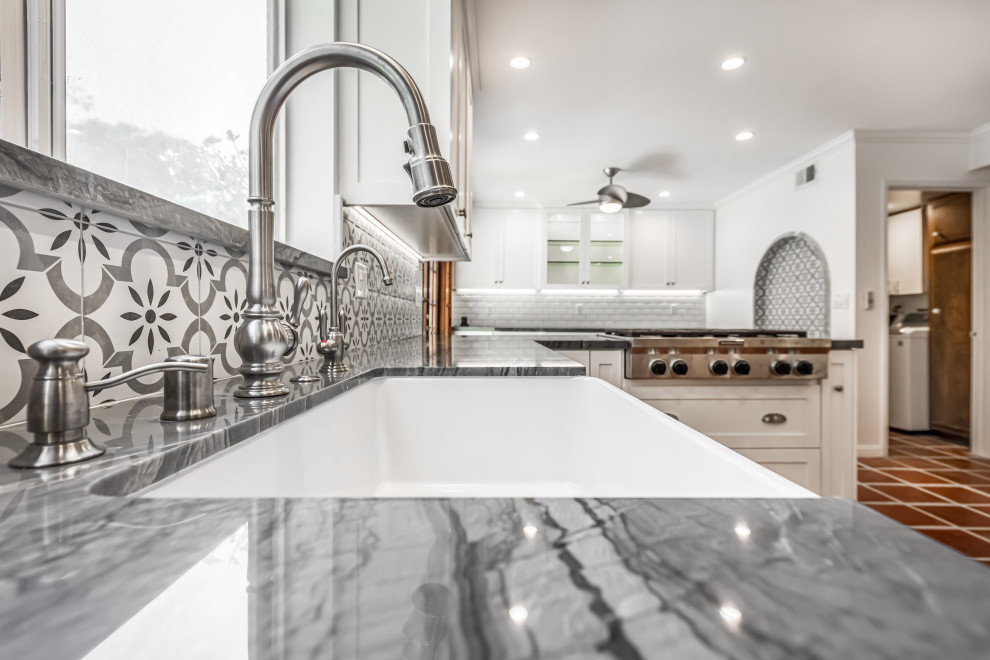 This is an example of a mid-sized country u-shaped open plan kitchen in Los Angeles with a farmhouse sink, shaker cabinets, white cabinets, quartzite benchtops, grey splashback, ceramic splashback, stainless steel appliances, terra-cotta floors, a peninsula, red floor and grey benchtop.