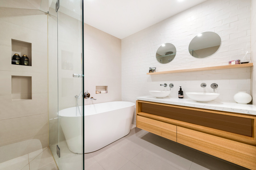 This is an example of a mid-sized contemporary master bathroom in Melbourne with flat-panel cabinets, beige cabinets, a freestanding tub, an open shower, beige tile, porcelain tile, white walls, porcelain floors, a vessel sink, beige floor, an open shower and white benchtops.