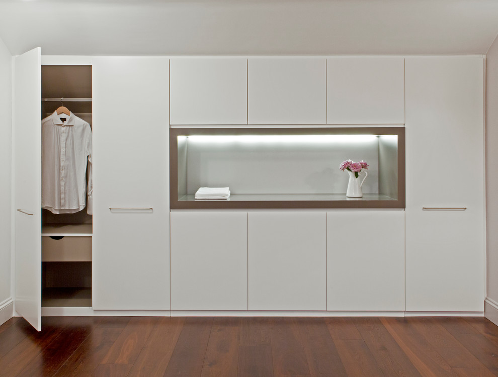 Photo of a contemporary gender-neutral built-in wardrobe in London with dark hardwood floors, recessed-panel cabinets and white cabinets.