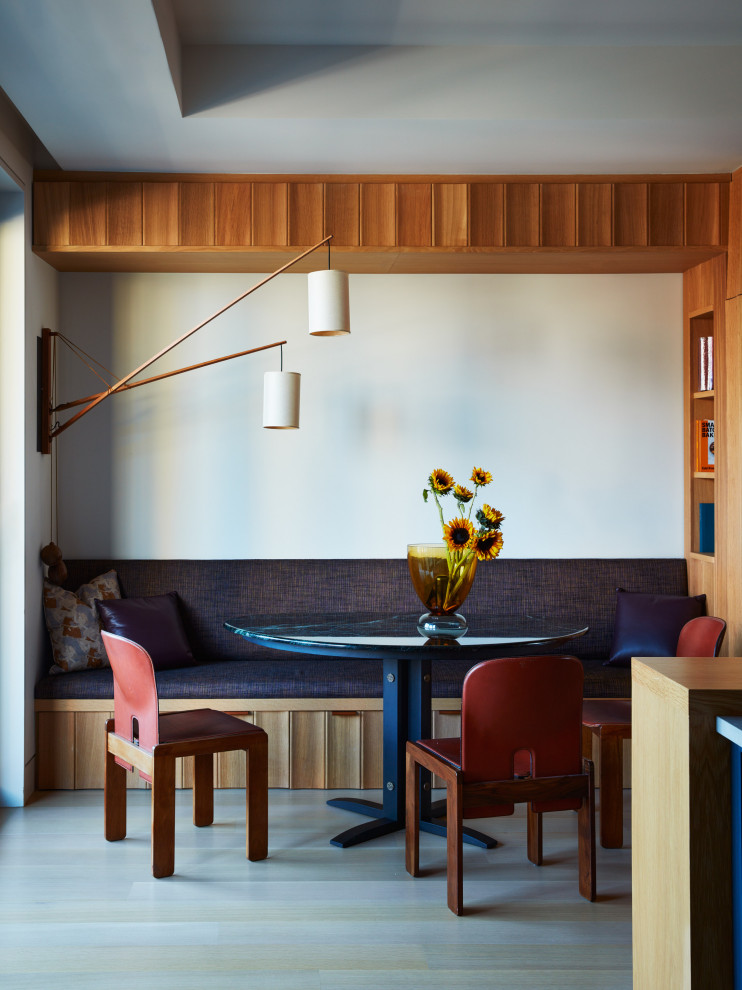 Cette image montre une petite salle à manger design avec une banquette d'angle, parquet clair et un mur blanc.