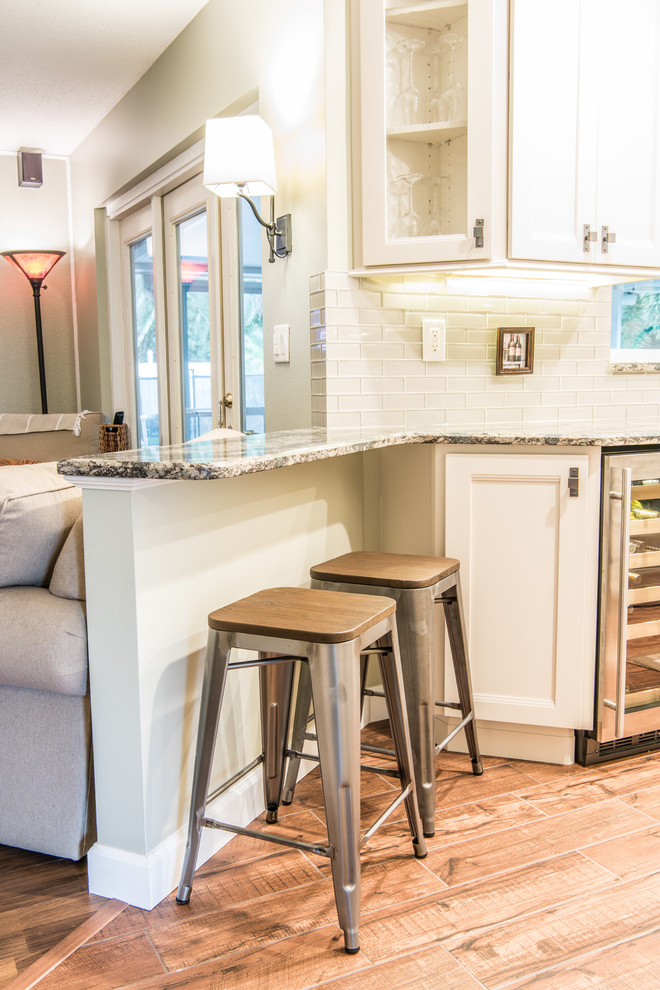 Eat-in kitchen - mid-sized transitional galley porcelain tile and brown floor eat-in kitchen idea with white cabinets, gray backsplash, glass tile backsplash, stainless steel appliances, shaker cabinets, quartz countertops and no island