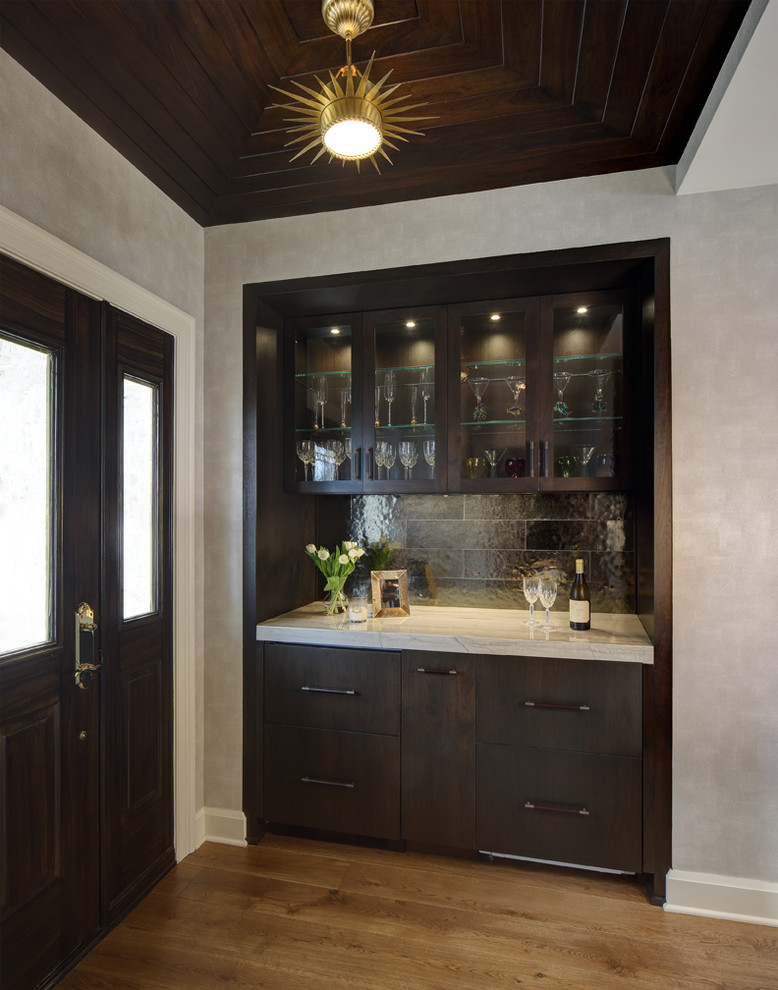 Photo of a small contemporary home bar in Cleveland with flat-panel cabinets, dark wood cabinets, marble benchtops, black splashback and light hardwood floors.