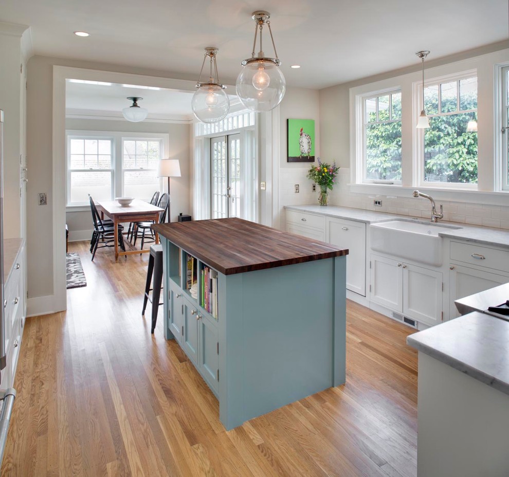 Inspiration for a mid-sized arts and crafts u-shaped eat-in kitchen in Portland with a farmhouse sink, shaker cabinets, white cabinets, marble benchtops, white splashback, subway tile splashback, stainless steel appliances, medium hardwood floors and with island.