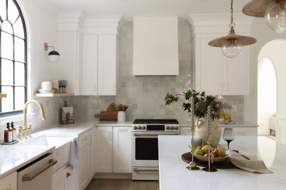This is an example of a mid-sized transitional single-wall open plan kitchen in Atlanta with a farmhouse sink, flat-panel cabinets, white cabinets, quartz benchtops, multi-coloured splashback, ceramic splashback, white appliances, medium hardwood floors, with island, beige floor and white benchtop.