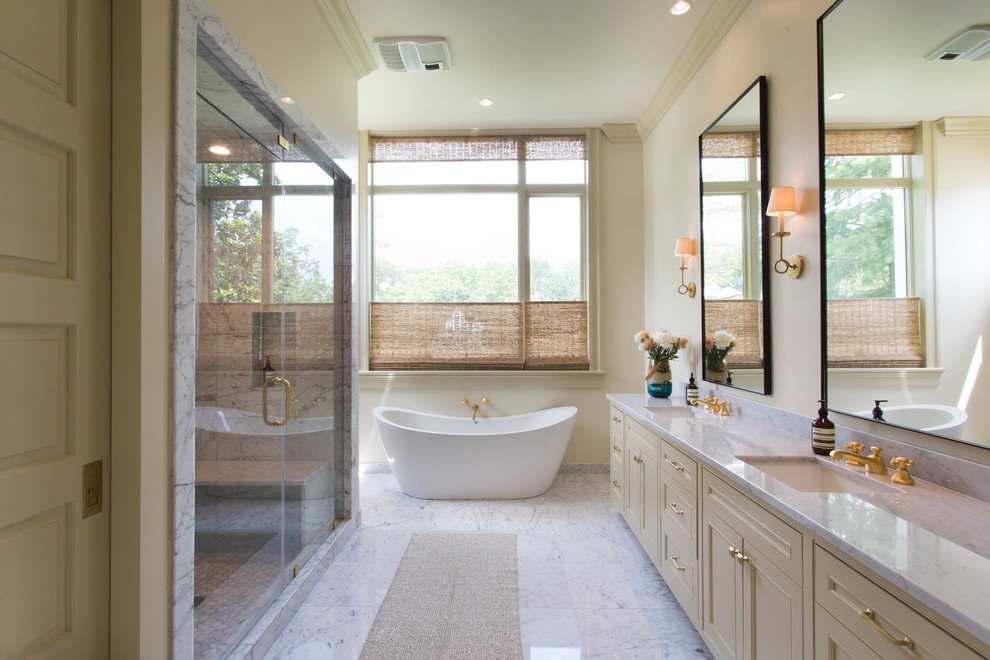 This is an example of a transitional master bathroom in New Orleans with beaded inset cabinets, beige cabinets, a freestanding tub, an alcove shower, marble, beige walls, marble floors, an undermount sink, marble benchtops, white floor, a hinged shower door and white tile.