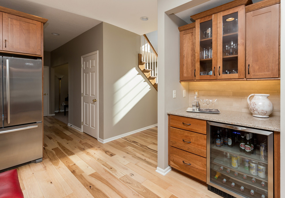 Open concept kitchen - mid-sized transitional l-shaped light wood floor open concept kitchen idea with an undermount sink, recessed-panel cabinets, medium tone wood cabinets, quartz countertops, beige backsplash, stone tile backsplash, stainless steel appliances and an island