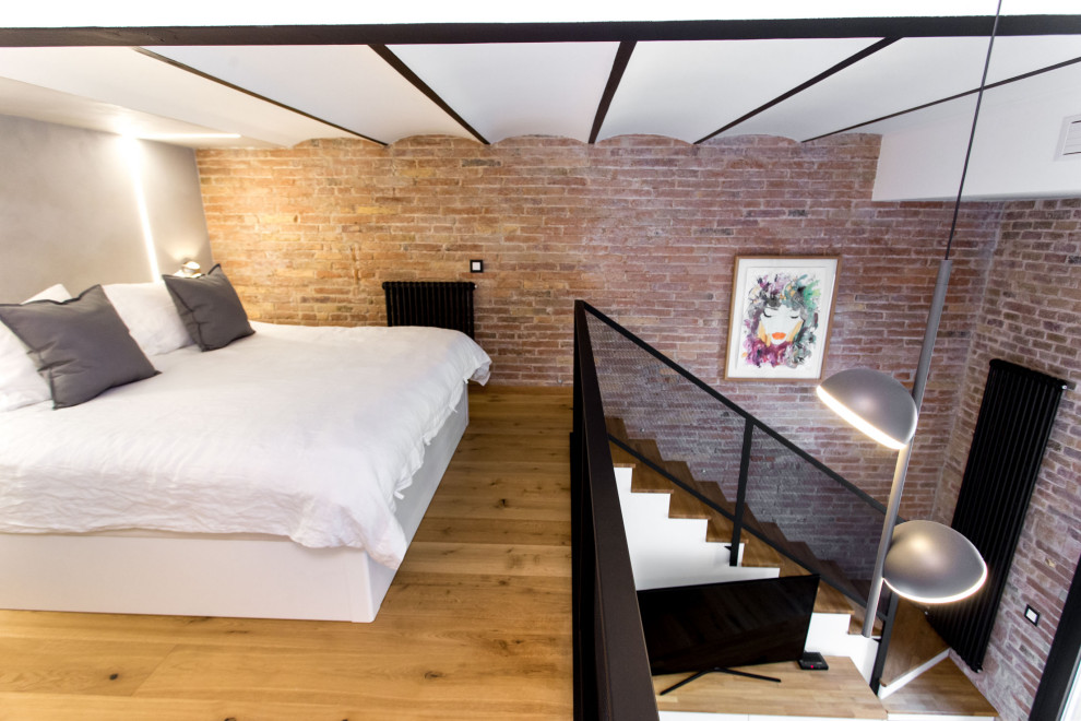 Design ideas for a small industrial loft-style bedroom in Barcelona with medium hardwood floors, vaulted and brick walls.