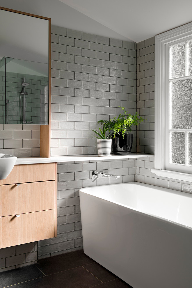 Contemporary bathroom in Brisbane with flat-panel cabinets, light wood cabinets, a freestanding tub, gray tile, subway tile, grey walls, a vessel sink, grey floor and white benchtops.