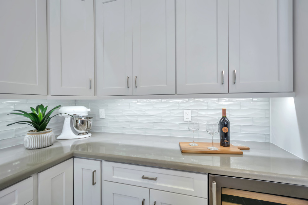Large transitional l-shaped porcelain tile and brown floor eat-in kitchen photo in Phoenix with a farmhouse sink, shaker cabinets, white cabinets, quartz countertops, white backsplash, subway tile backsplash, stainless steel appliances, an island and gray countertops