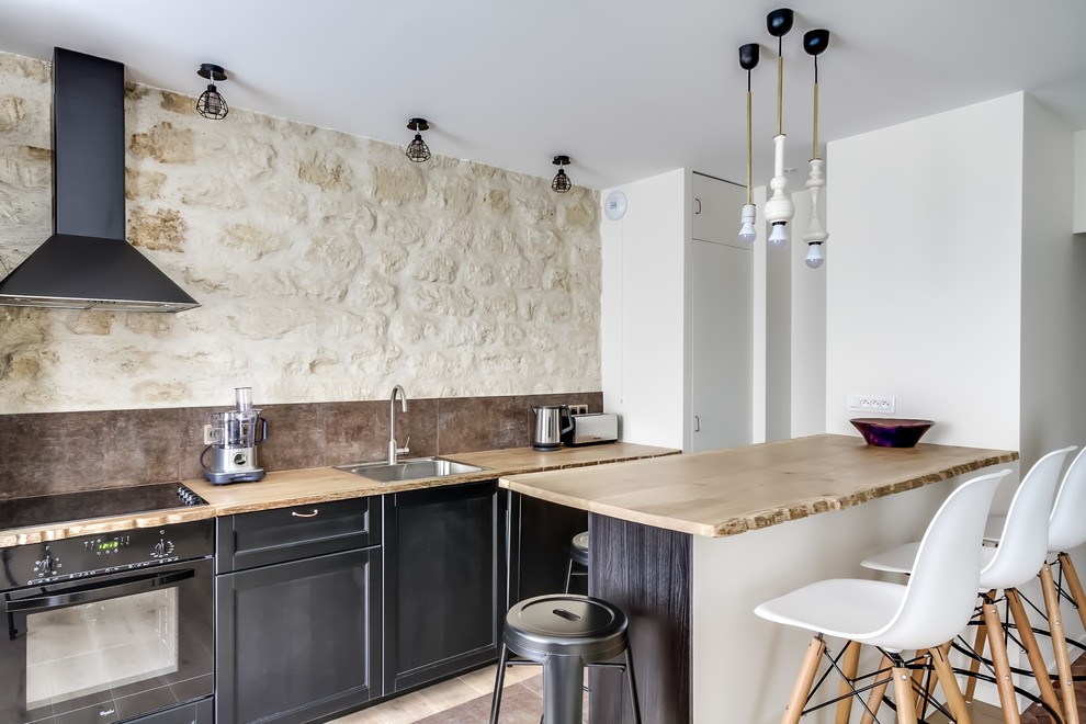 Inspiration for a mid-sized country galley eat-in kitchen in Paris with a single-bowl sink, recessed-panel cabinets, black cabinets, wood benchtops, brown splashback, black appliances and with island.