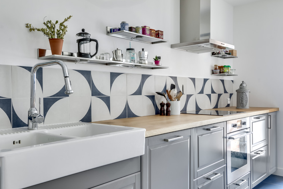This is an example of a mid-sized galley eat-in kitchen in Paris with wood benchtops, blue splashback, blue floor, a double-bowl sink, raised-panel cabinets, grey cabinets, cement tile splashback, stainless steel appliances, ceramic floors and no island.