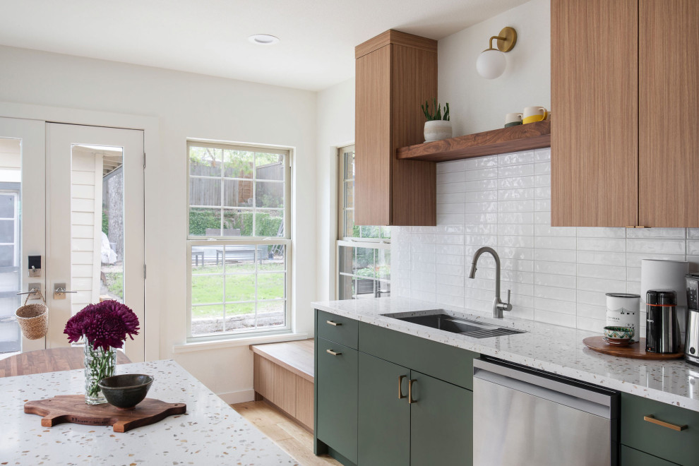Mid-sized transitional galley light wood floor and brown floor open concept kitchen photo in Austin with an undermount sink, flat-panel cabinets, green cabinets, terrazzo countertops, white backsplash, porcelain backsplash, stainless steel appliances, an island and multicolored countertops