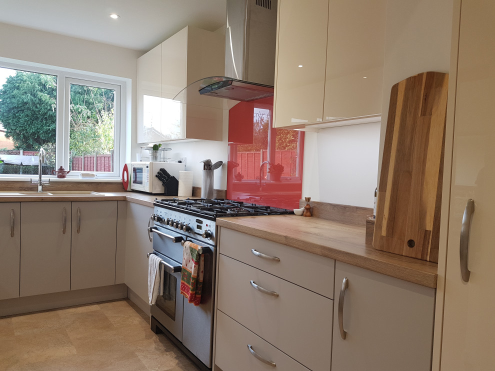 This is an example of a small contemporary u-shaped separate kitchen in West Midlands with a double-bowl sink, flat-panel cabinets, beige cabinets, laminate benchtops, orange splashback, glass sheet splashback, black appliances, vinyl floors, no island, brown floor and brown benchtop.