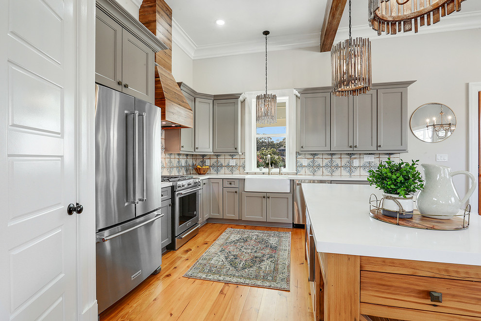 Photo of a transitional l-shaped kitchen in New Orleans with a farmhouse sink, shaker cabinets, grey cabinets, multi-coloured splashback, stainless steel appliances, medium hardwood floors, with island, brown floor and white benchtop.