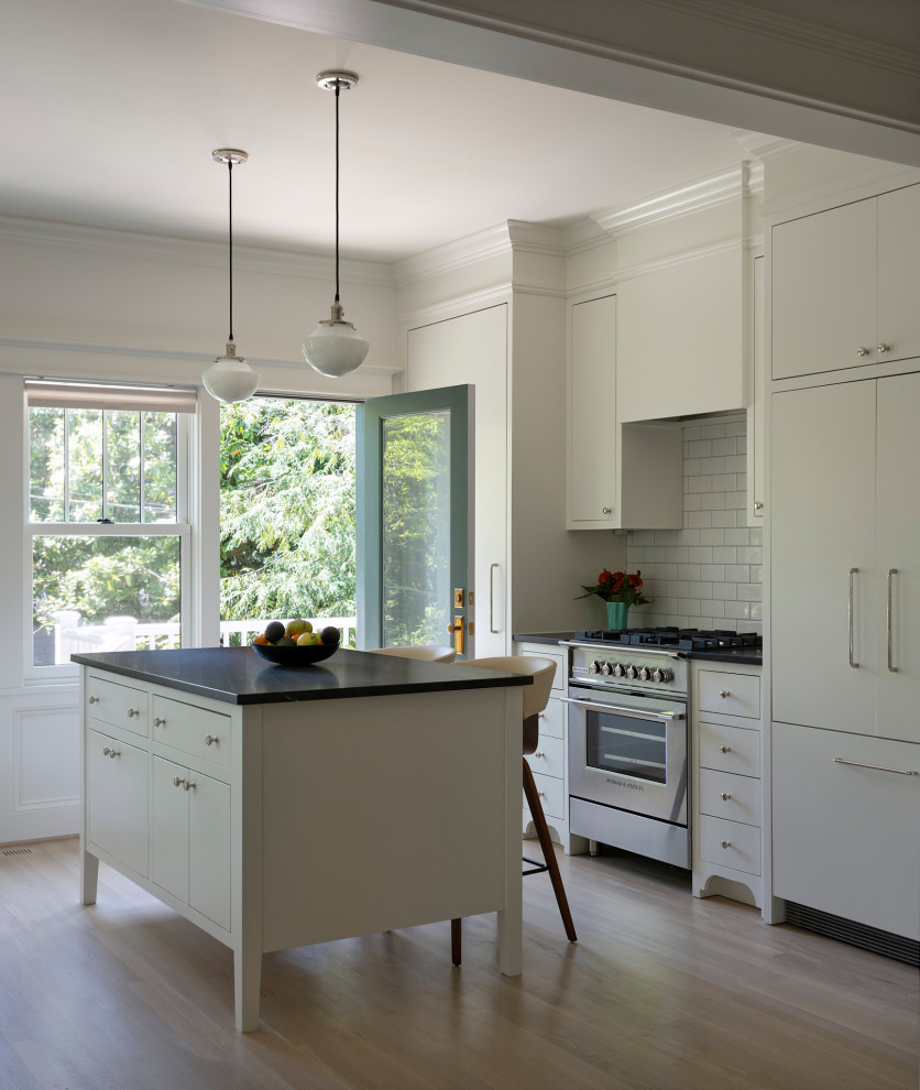 Inspiration for a transitional galley light wood floor and beige floor kitchen remodel in DC Metro with white cabinets, granite countertops, white backsplash, paneled appliances, an island, black countertops, flat-panel cabinets and subway tile backsplash