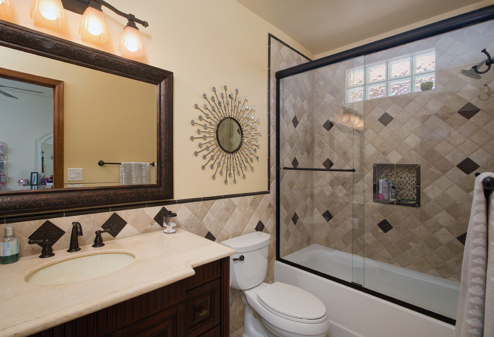 Design ideas for a mid-sized transitional 3/4 bathroom in Phoenix with raised-panel cabinets, dark wood cabinets, an alcove tub, a shower/bathtub combo, beige tile, stone tile, an undermount sink and limestone benchtops.