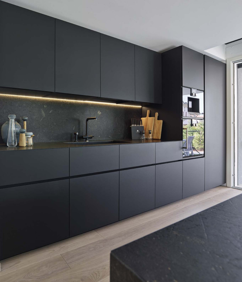 На фото: параллельная кухня среднего размера в стиле модернизм с одинарной мойкой, плоскими фасадами, черными фасадами, черным фартуком, черной техникой, светлым паркетным полом, островом, черной столешницей и многоуровневым потолком