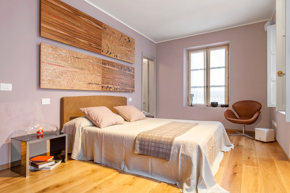 This is an example of a large contemporary master bedroom in Milan with pink walls and light hardwood floors.