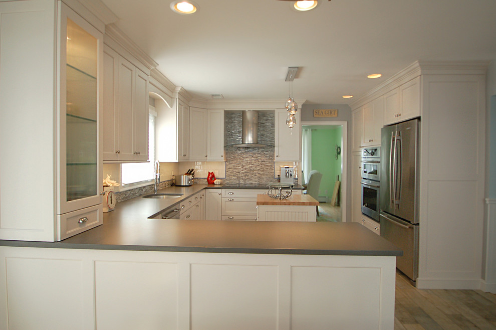 This is an example of a mid-sized traditional u-shaped eat-in kitchen in New York with an undermount sink, recessed-panel cabinets, white cabinets, quartz benchtops, grey splashback, mosaic tile splashback, stainless steel appliances, light hardwood floors and multiple islands.